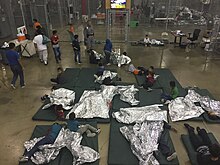 Children and juveniles in a wire mesh compartment, showing sleeping mats and thermal blankets on floor