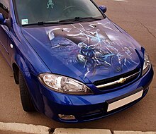 Blue Chevrolet car with a spray-painted mural on the hood. Mural depicts two men fighting with glowing swords.