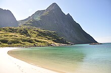 Foto eines Sandstrandes, der in einen Berg mit steil abfallender Küstenseite übergeht