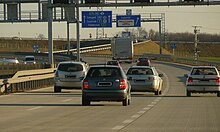 A view of the motorway from a carriageway, showing three traffic lanes and directional traffic signs mounted in a gantry