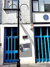 Photo de l'entrée d'un immeuble aux murs blancs, fermée par de grandes grilles bleues