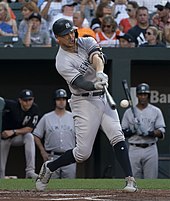 A baseball player taking a swing. He is wearing a gray jersey and a dark blue batting helmet that has a white interlocking "N" and "Y" logo.