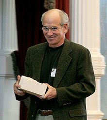 Sachar shown from the waist up, smiling, and holding a small box.