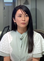 A Japanese woman with long hair and wearing a green and white shirt