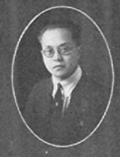 A black and white photograph of Wing Sam Chinn wearing a suit and glasses.