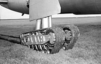 The experimental tracked landing gear unit of an XB-36, consisting of 2 flexible tracks supported by wheels, is pictured stopped in short grass with ruts trailing behind it.