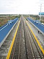 A south facing picture of the Boca Raton Tri-Rail station. A northbound Amtrak train is visible in the distance.