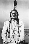 American Indian sitting with long pony tails and a single feather in hair