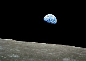 Photo taken from lunar orbit, moon surface in foreground, Earth rising in background