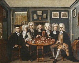 Six University College fellows in a well-decorated room sit around a table, which holds flute glasses, tobacco pipes, a candle, and a bottle of red liquid. All the men wear black robes and white periwigs. The centre and left-most men (Thomas and John Cockman) wear mortarboards.