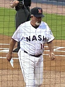 A man in a white baseball uniform with "NASH" written in navy letters across the chest, a red "16" below, and a navy cap with a red and white "N" on the front walking to the dugout