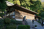 A rather wide building with wooden beams and white painted walls. The front wall is completely covered by wooden grill windows.