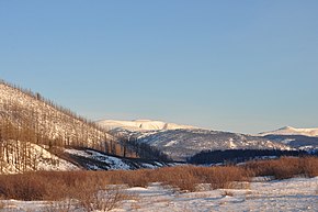 Photograph of a landscape in winter, with trees bare, and valleys and mountains covered in snow.