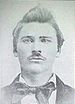 Head of a young white man with a thin mustache and hair pointing straight up from his forehead, wearing a large bowtie.