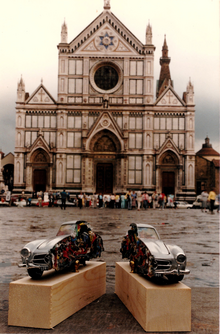 l'opera rappresenta un modello di auto in scala ridotta riempito di rifiuti e sezionato longitudinalmente, davanti la basilica di Santa Croce a Firenze