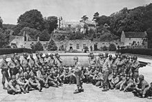 A group of American soldiers posing in front of a swimming pool, with terraced gardens behind them and a castle at the top of the terraces.