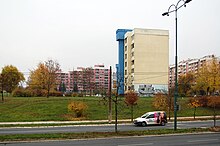 Une tour jaune, une tour bleue, une barre orange et une barre rose, ainsi que des larges pelouses et une rue en avant-plan.