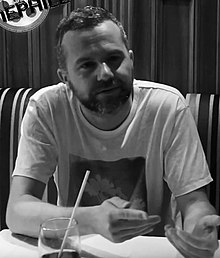 A black-and-white photo of a man in a t-shirt sat in a restaurant booth.