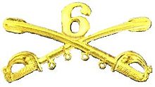 A computer generated reproduction of the insignia of the Union Army 6th Regiment cavalry branch. The insignia is displayed in gold and consists of two sheafed swords crossing over each other at a 45-degree angle pointing upwards with a Roman numeral 6