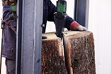 Photo d'un tronçon de chêne fendu avec un coin enfoncé par une fendeuse hydraulique.