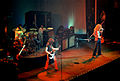 A colour photograph of the four members of Led Zeppelin performing onstage, with some other figures visible in the background (from British rhythm and blues)