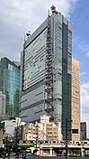 Ground-level view of a blue, glass, rectangular high-rise; attached to one side of the building are two structures consisting of poles that run the height of the building