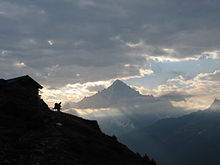 A walker silhouetted by a cabin on mountain slope