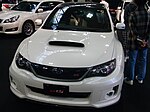 Subaru WRX STI tS, a lightened variant of the standard Subaru WRX STI sedan. This photo shows the front of the car, which is white; the car has been lightened by replacing the standard roof panel with carbon fiber, which is visible.