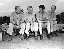 Photographie de quatre hommes en uniformes débraillés assis sur un petit banc.