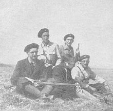 Des hommes en arme, coiffés de bérets, assis dans l'herbe.