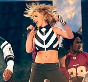 A female performer in a black-and-white ensemble, holding a microphone near her mouth