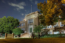 A three story school brick building. The school sign and green lawn reside in front of it