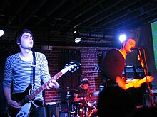 Several men performing onstage, playing instruments and singing into a microphone