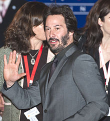 Reeves, dressed in a grey suit, waving to the crowd at the Berlin Film Festival, February 2009