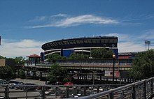 View from the Mets-Willets Point station's platform, with the former Shea Stadium in the background. A black fence, which surrounds the platform, is visible on the bottom right corner.