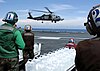 Four U.S. sailors in foreground prepare to load a pallet of purified water jugs onto an approaching SH-60B Seahawk helicopter from squadron HSL-47 landing on the flight deck of the nuclear-powered aircraft carrier USS Abraham Lincoln operating in the Indian Ocean off the waters of Indonesia and Thailand.