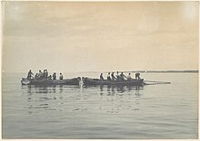 two boats with over 12 men pulling in fishing nets in calm water