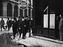 Photo en noir et blanc d'un groupe d'hommes en manteaux et cravates arrivant à l’angle d'une rue