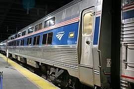 Stainless steel passenger rail car with a blue stripe and two thinner red stripes at window level