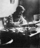 Black and white photo of man seated, drawing at a desk