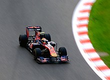 A navy blue and red Formula One car being driven at speed on a dry circuit