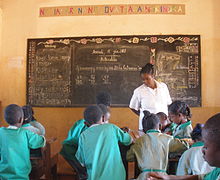 Malagasy children in green school uniforms working in groups as a teacher in white looks on