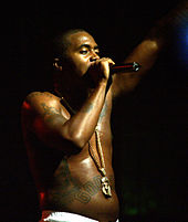 A barebodied Nas singing onstage.