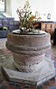 A circular sandstone font standing on an octagonal base, bearing a floral decoration