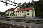 Foto eines Bahnhofsgebäudes mit Gleisen im Vordergrund.