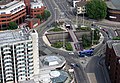 Aerial view of roundabout, a junction of several streets. Vehicles traverse around the roundabout, which is surrounded by buildings, mostly multi-storey (from Transport)