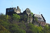 Photographie d'un château partiellement ruiné situé au sommet d'une colline boisée.