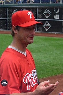 A man wearing a red baseball jersey and cap holds out his right hand