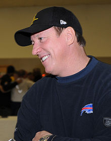 Jim Kelly in a hat and Buffalo Bills sweater smiling.