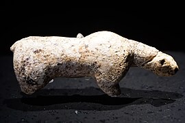 Photographie en couleurs sur fond noir et vue du dessus d'une statuette en ivoire représentant un ours des cavernes, ses pattes amputées reposant sur un socle de verre.